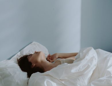 Peaceful scene of a woman sleeping in a soft bed with white linens indoors.