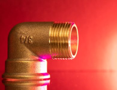 Close-up of a shiny brass pipe elbow fitting against a vibrant red backdrop, showcasing industrial elegance.