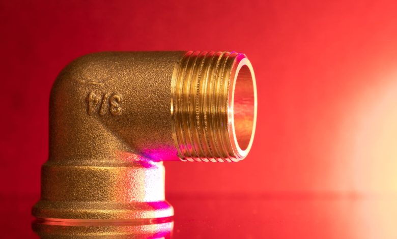 Close-up of a shiny brass pipe elbow fitting against a vibrant red backdrop, showcasing industrial elegance.