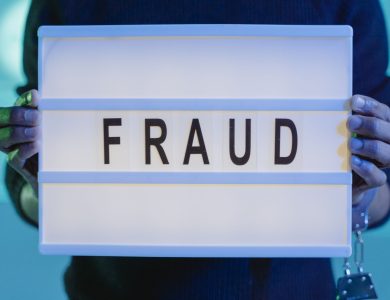 Close-up of hands holding a sign with 'fraud', illuminated in blue light.