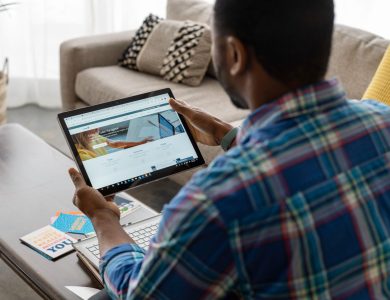 Man with plaid shirt browsing internet on tablet at home, seated on sofa.