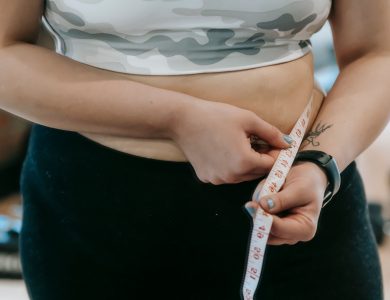 Crop anonymous plus size female with measuring tape measuring waist on blurred background