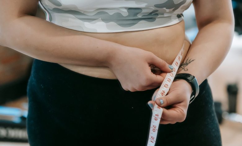 Crop anonymous plus size female with measuring tape measuring waist on blurred background
