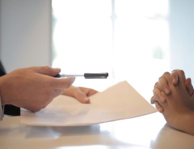 Side view of faceless formal man giving pen and paper to focused female with clenched hands at table on meeting