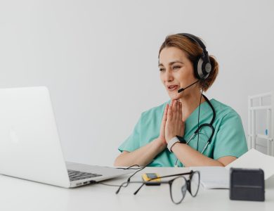 Female nurse using telemedicine for a virtual consultation on a laptop, wearing headphones and stethoscope.
