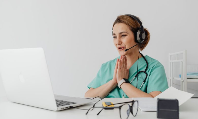 Female nurse using telemedicine for a virtual consultation on a laptop, wearing headphones and stethoscope.
