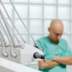 Close-up of dental tools with a blurred dentist in scrubs in the background.