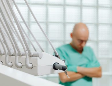 Close-up of dental tools with a blurred dentist in scrubs in the background.
