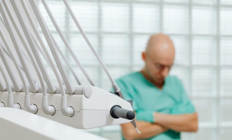 Close-up of dental tools with a blurred dentist in scrubs in the background.