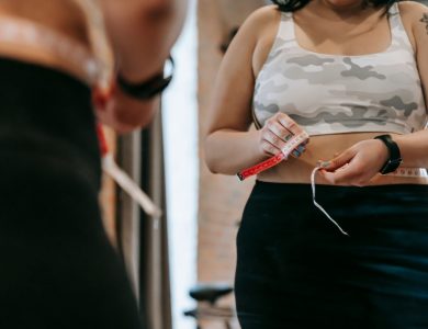 Low angle of crop faceless overweight female in activewear reflecting in mirror in sports club