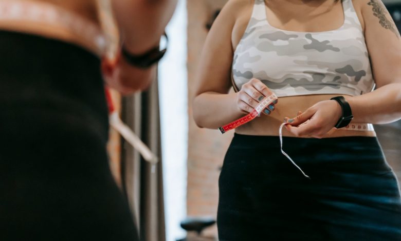 Low angle of crop faceless overweight female in activewear reflecting in mirror in sports club
