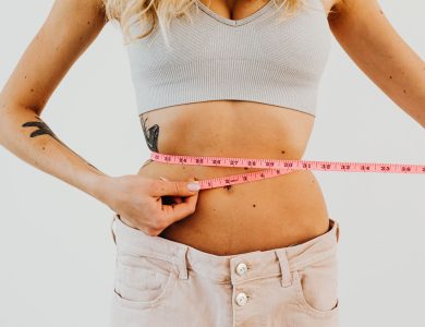 Close-up of woman in sports bra measuring waist with pink tape for fitness goals.