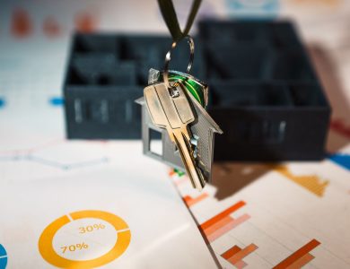 Real estate keys on house keychain with financial graphs, symbolizing property investment.
