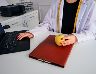 A dietician sitting at a desk with a laptop and apple, symbolizing healthy working lifestyle.