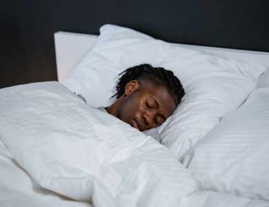 A young man resting peacefully in a bed with white sheets and a dark background.
