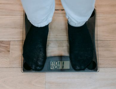 From above of crop unrecognizable plus size person in casual clothes standing on weighing scale on wooden floor