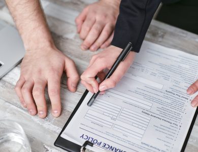 Close-up image of two people signing an insurance policy document on a wooden desk.