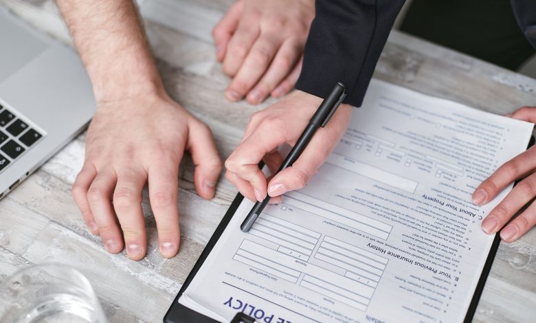 Close-up image of two people signing an insurance policy document on a wooden desk.
