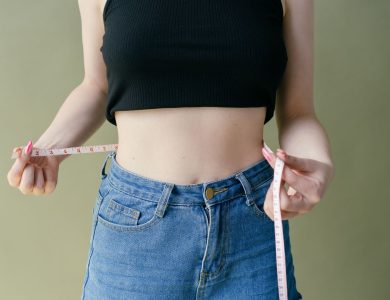 A woman in denim and crop top using measuring tape for waist check.