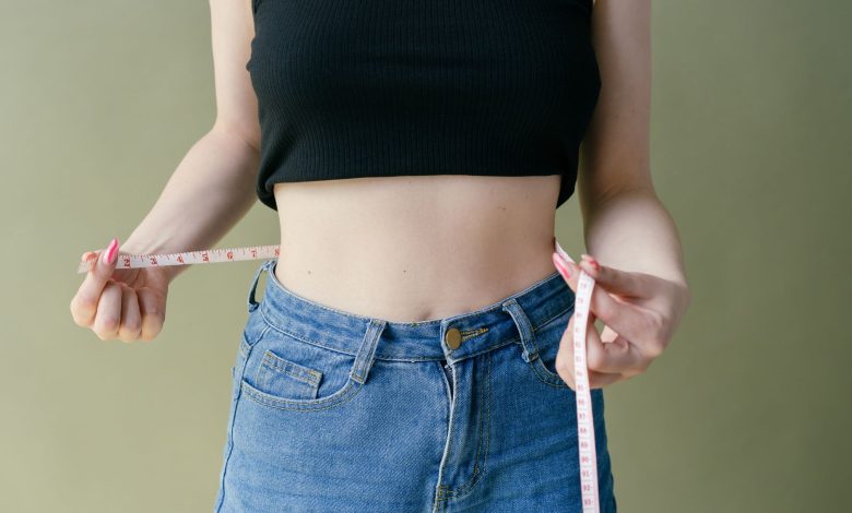 A woman in denim and crop top using measuring tape for waist check.