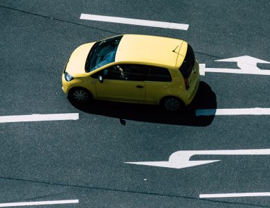 Aerial view of a yellow car on a road with directional arrows, highlighting urban transport.