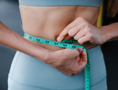 Close-up of a woman measuring her waist with a tape, representing fitness, health, and weight loss.