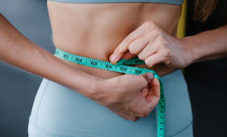 Close-up of a woman measuring her waist with a tape, representing fitness, health, and weight loss.