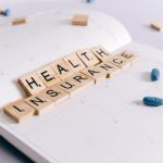 Scrabble tiles spelling 'Health Insurance' on a calendar with pills.