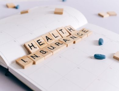 Scrabble tiles spelling 'Health Insurance' on a calendar with pills.