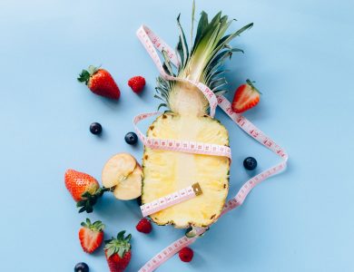 Fresh fruits with tape measure on blue background symbolize healthy lifestyle and nutrition.