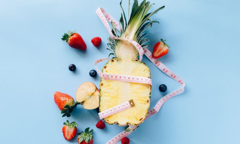 Fresh fruits with tape measure on blue background symbolize healthy lifestyle and nutrition.