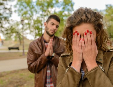 A young man apologizes while a woman covers her face, set in an outdoor park.