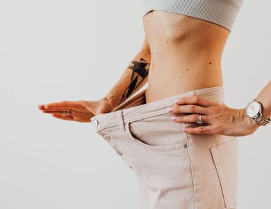 Close-up of a woman in oversized pants showcasing weight loss progress. Studio shot with neutral background.