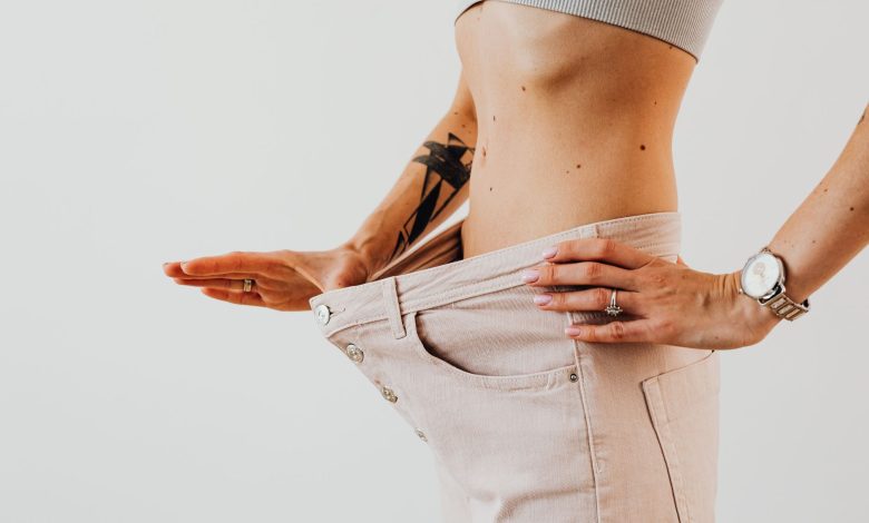 Close-up of a woman in oversized pants showcasing weight loss progress. Studio shot with neutral background.