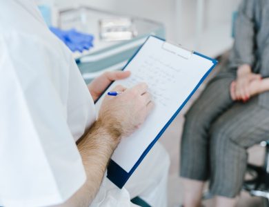 Medical professional writing patient notes on clipboard during consultation.