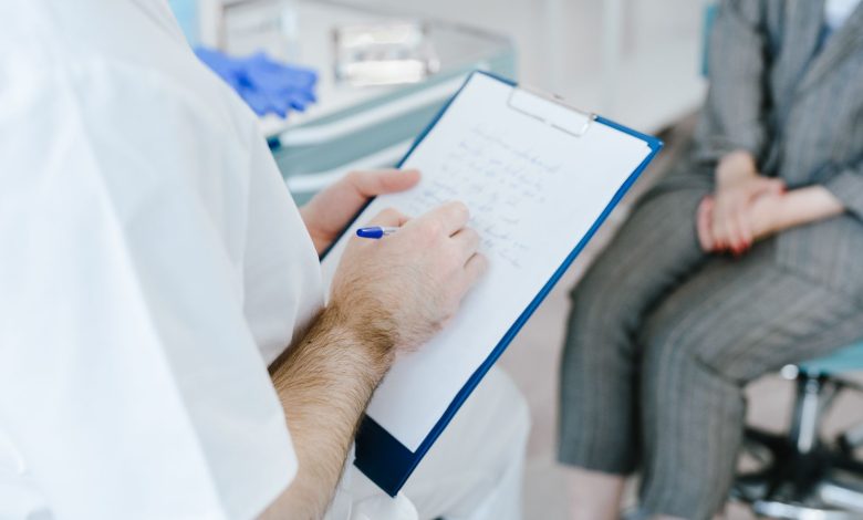 Medical professional writing patient notes on clipboard during consultation.