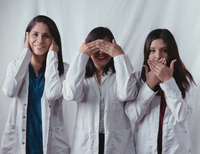 Three women scientists in lab coats posing playfully, symbolizing see no evil, hear no evil, speak no evil.