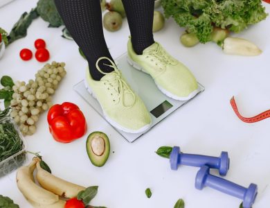 Person standing on scales surrounded by fresh produce and fitness equipment symbolizing a balanced lifestyle.