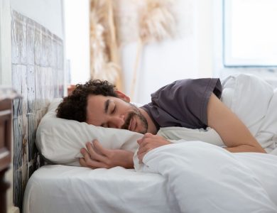 Man resting peacefully in bed, wrapped in white sheets, creating a serene and cozy atmosphere.