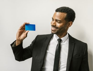 A confident man in a suit holds a credit card, smiling towards it.
