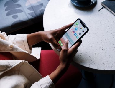A person checks social media apps on a smartphone while sitting at a café table.