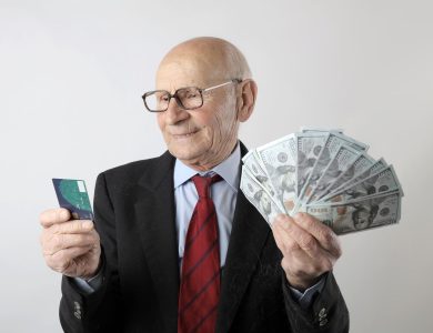 Elderly man in a suit holding a credit card and US dollar bills, representing finance and wealth.