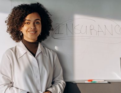 African American woman smiling in office setting with a whiteboard displaying 'Insurance'.