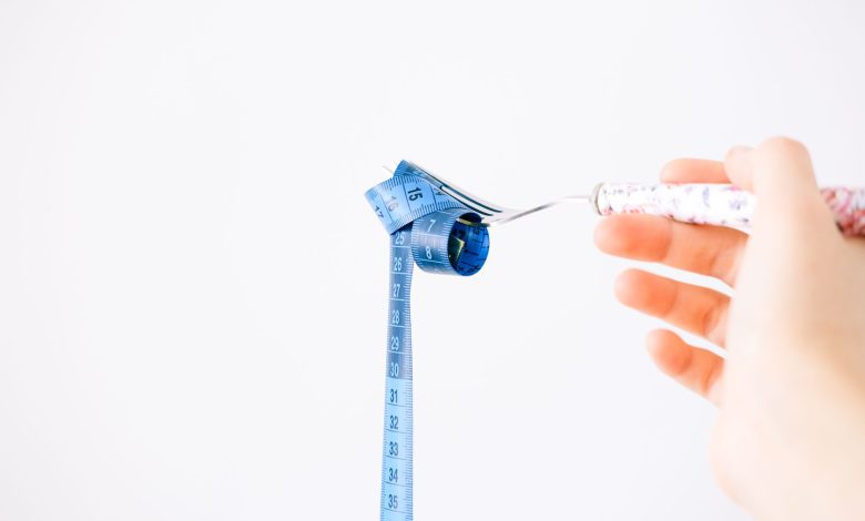 A blue measuring tape wrapped around a fork representing dieting or healthy eating concept.